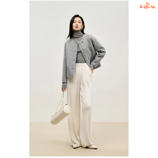 Woman wearing a gray sweater and white pants holding a white bag on a plain background