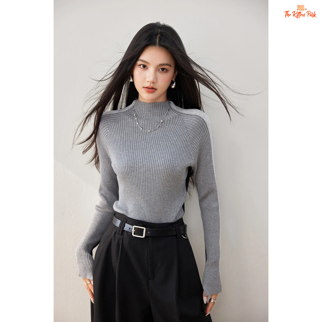 Woman wearing a gray ribbed sweater and black pants against a plain background