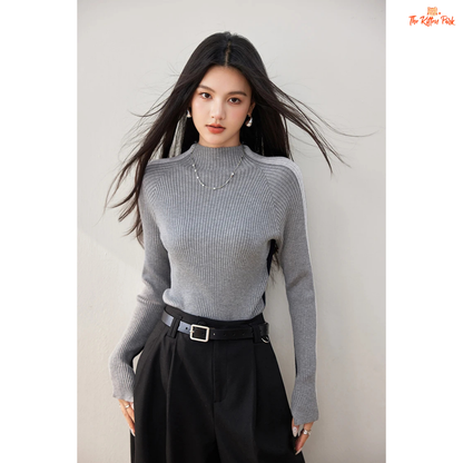 Woman wearing a gray ribbed sweater and black pants against a plain background