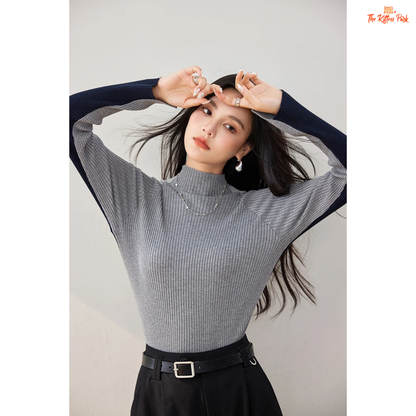 Woman wearing a gray ribbed sweater and black skirt against a plain background