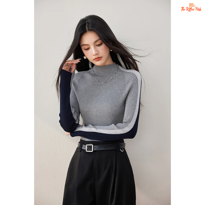 Woman wearing a gray and navy sweater with black pants against a plain background