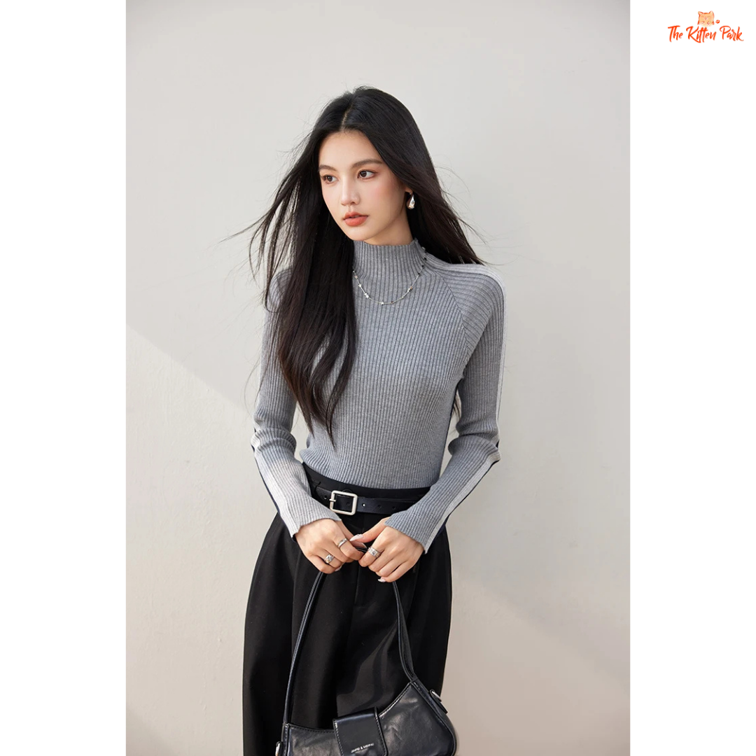 Woman wearing a gray turtleneck and black pants against a plain background