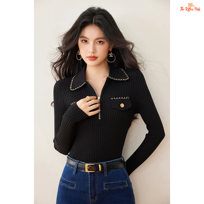 Woman wearing a black ribbed sweater with chain details and blue jeans against a plain background