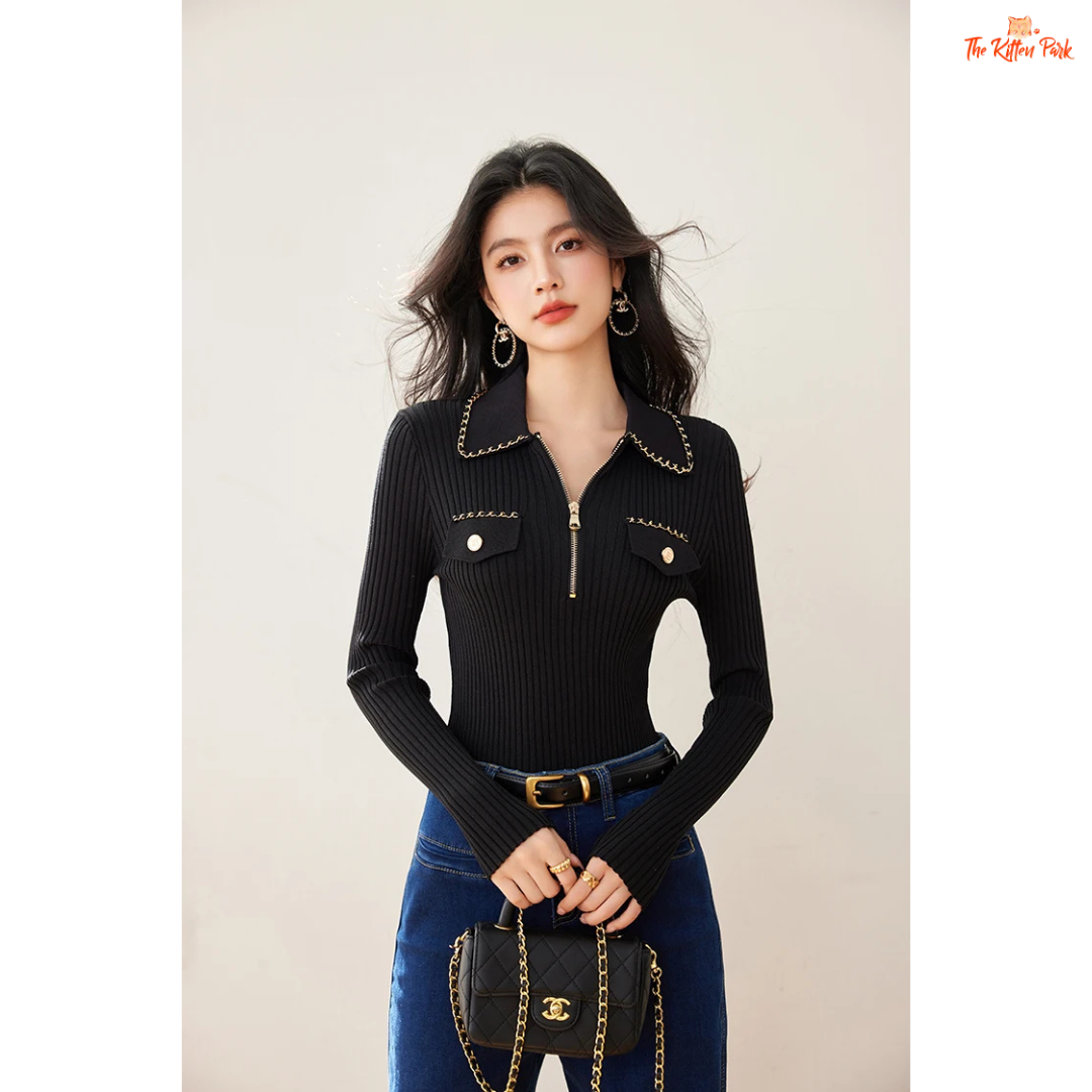 Woman wearing a black ribbed sweater with gold accents and blue jeans, holding a black handbag.