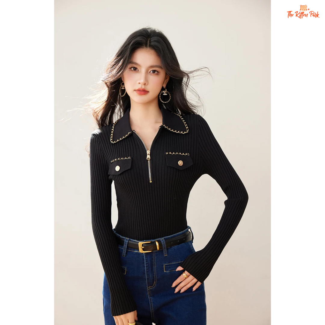 Woman wearing a black ribbed sweater with chain details and blue jeans on a plain background