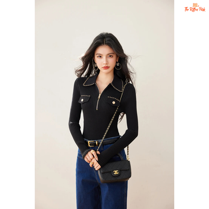 Woman wearing a black ribbed sweater with chain details and blue jeans on a beige background