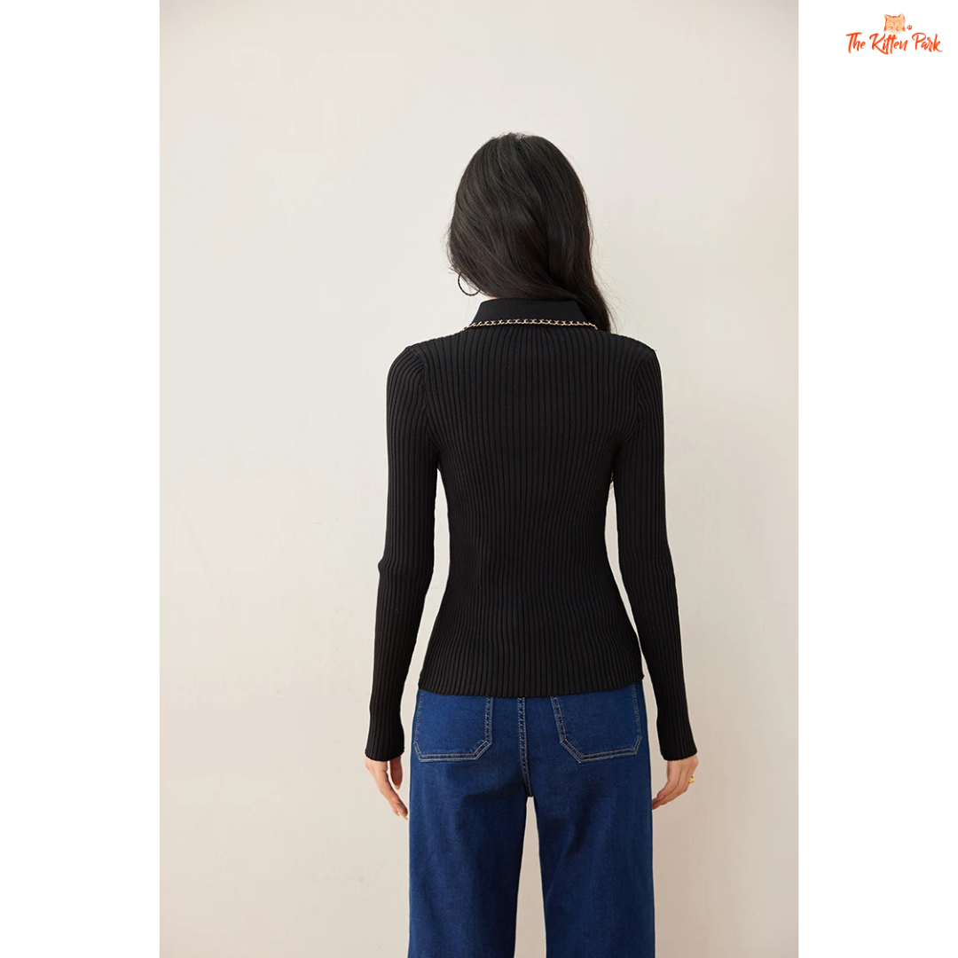 Woman wearing a black ribbed sweater with chain details and blue jeans on a beige background