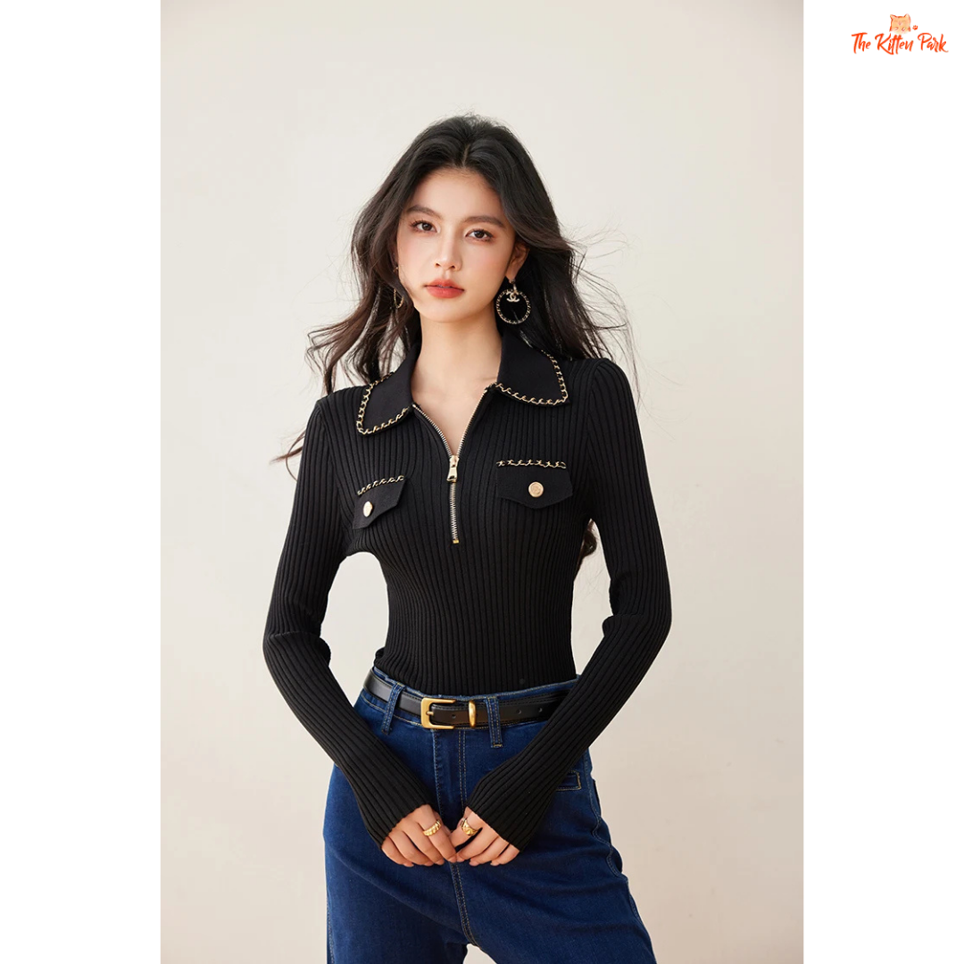 Woman wearing a black ribbed sweater with chain details and blue jeans on a beige background