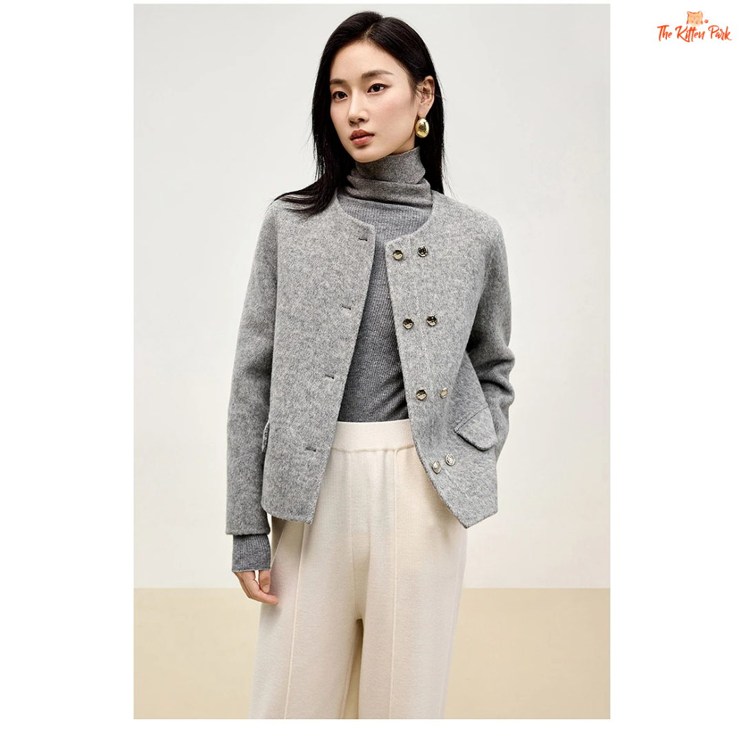 Woman wearing a gray coat over a gray turtleneck and white pants on a plain background