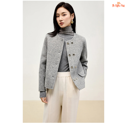 Woman wearing a gray coat over a gray turtleneck and white pants on a plain background