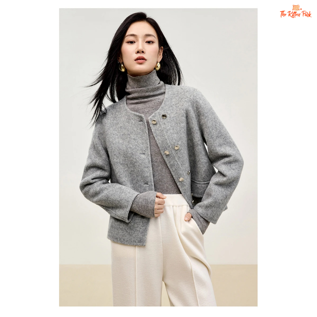 Woman wearing a gray cardigan over a turtleneck sweater with white pants on a plain background