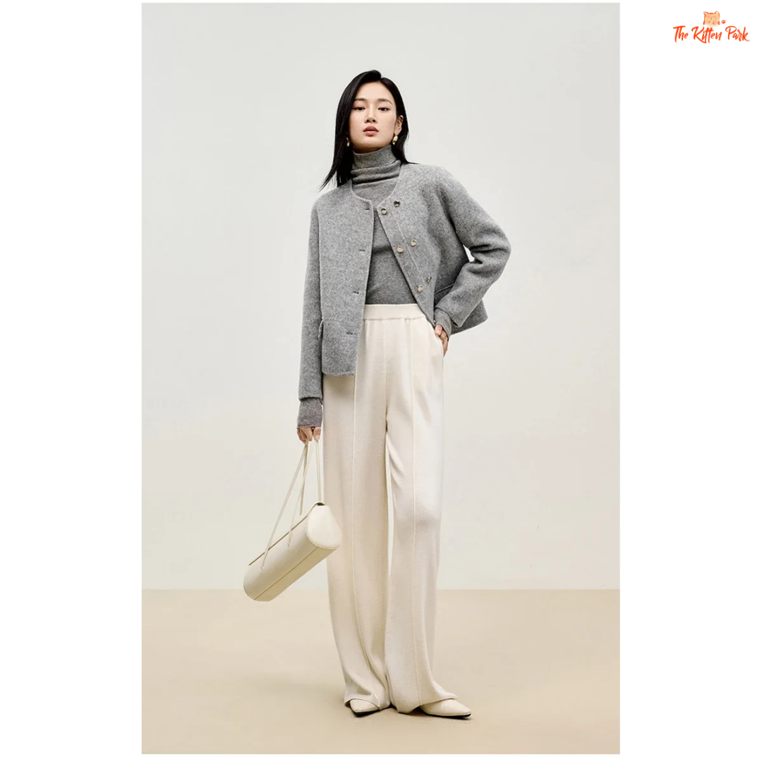 Woman wearing a gray sweater and white pants holding a white bag on a plain background