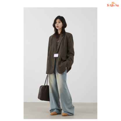 Person wearing a brown blazer and light blue jeans with a handbag on a plain background