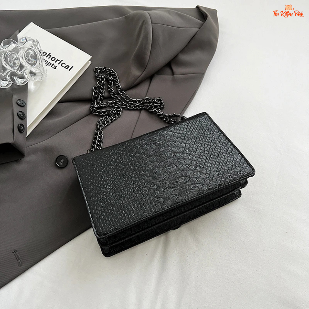 Small square crossbody bag with retro snake pattern, chain strap, hard shell body, and zippered interior for a bold fashion statement.