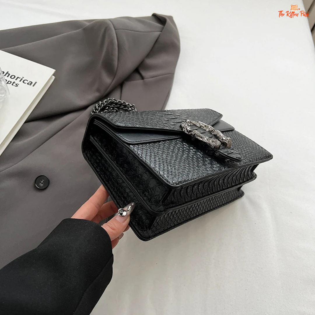 Small square crossbody bag with retro snake pattern, chain strap, hard shell body, and zippered interior for a bold fashion statement.