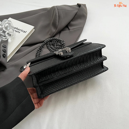 Small square crossbody bag with retro snake pattern, chain strap, hard shell body, and zippered interior for a bold fashion statement.