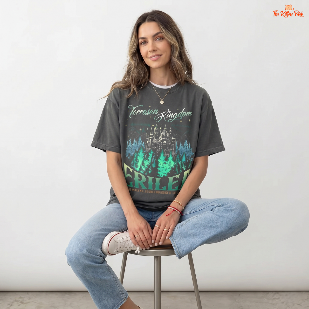 Woman wearing a t-shirt with a castle graphic and text, sitting on a stool against a white background.