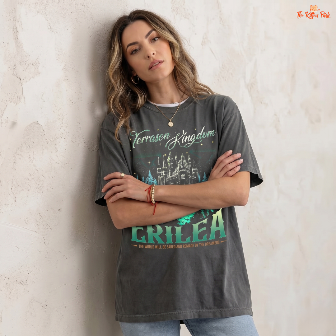 Woman wearing a dark gray t-shirt with colorful graphics and text, standing against a light textured wall.