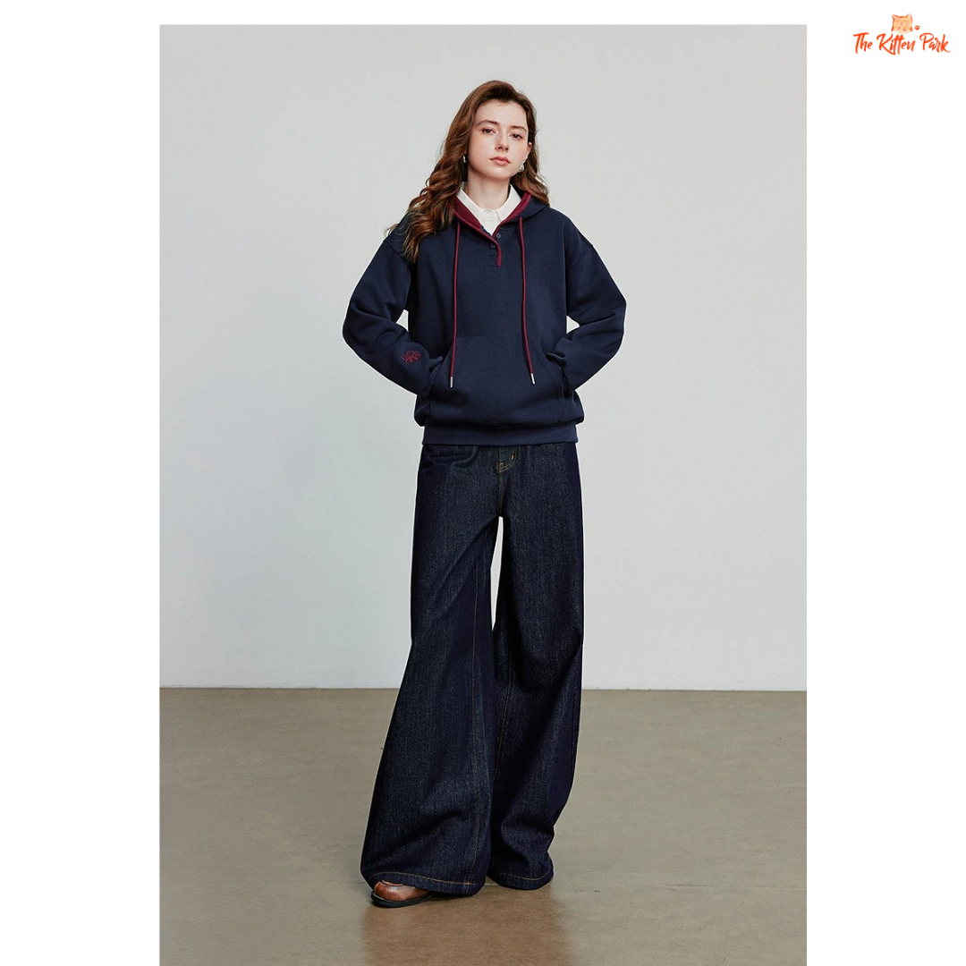 Person wearing a navy blue hoodie and wide-leg jeans against a plain background