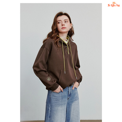 Person wearing a brown hoodie with a logo and blue jeans against a plain background