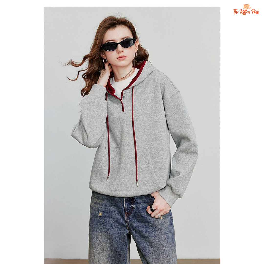 Person wearing a gray hoodie with red accents and blue jeans against a plain background