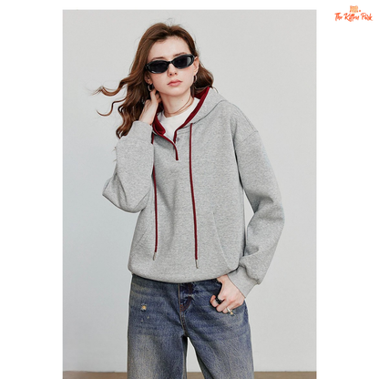 Person wearing a gray hoodie with red accents and blue jeans against a plain background