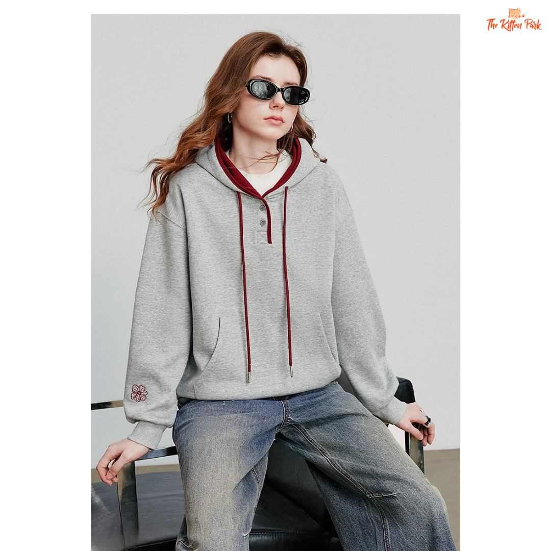 Person wearing a gray hoodie with red accents and blue jeans, sitting on a chair.