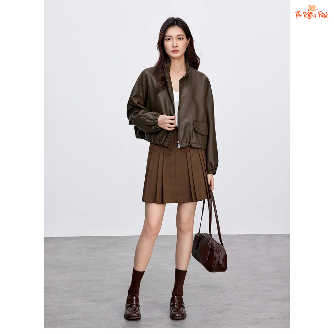 Woman wearing a brown leather jacket and skirt holding a matching handbag on a white background