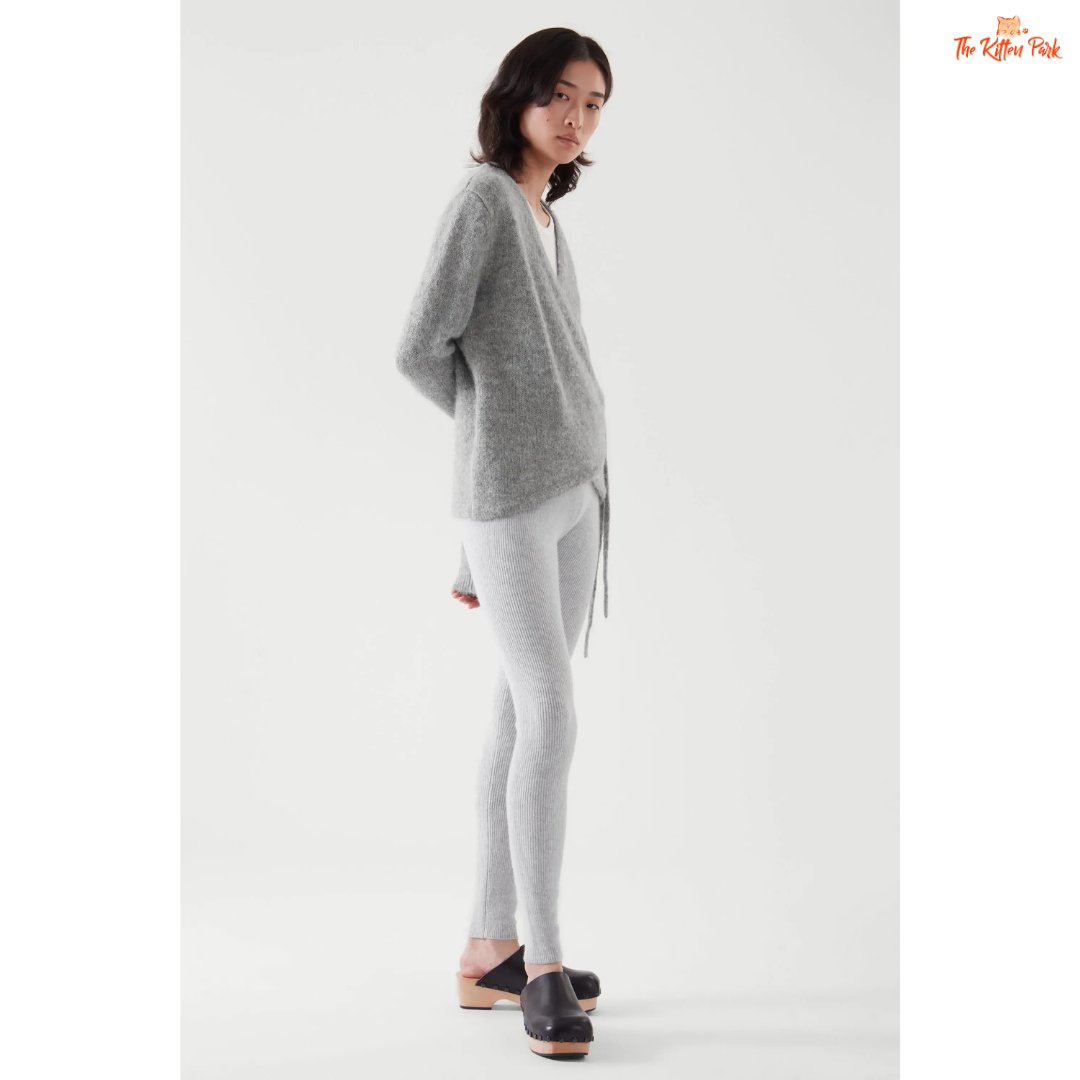 Woman wearing a gray cardigan and white pants on a white background