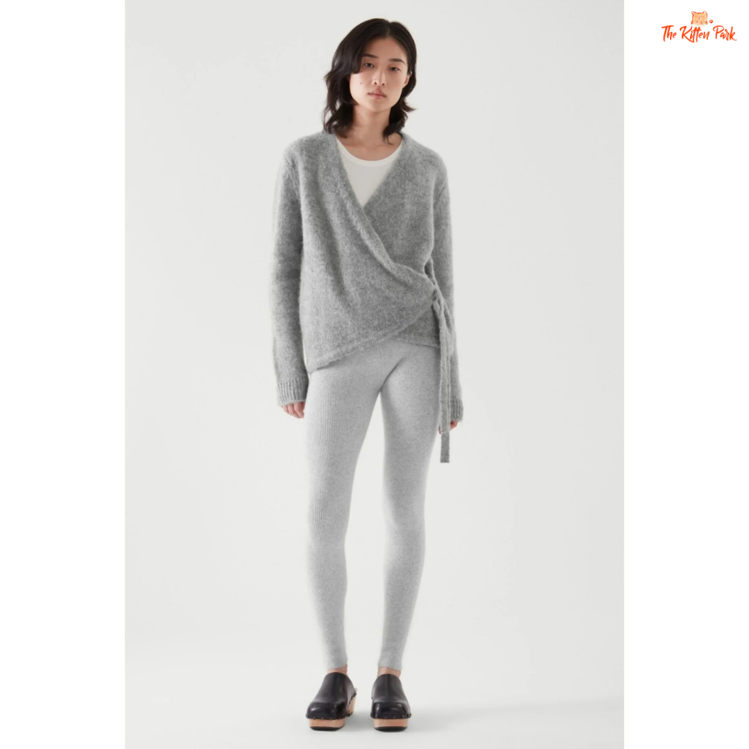 Woman wearing a gray knit cardigan and leggings on a white background