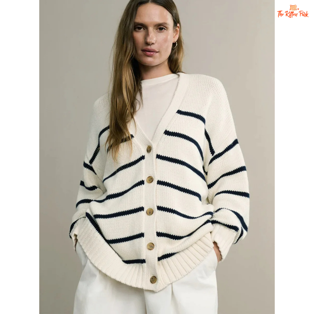 Woman wearing a cream cardigan with navy stripes and gold buttons on a plain background