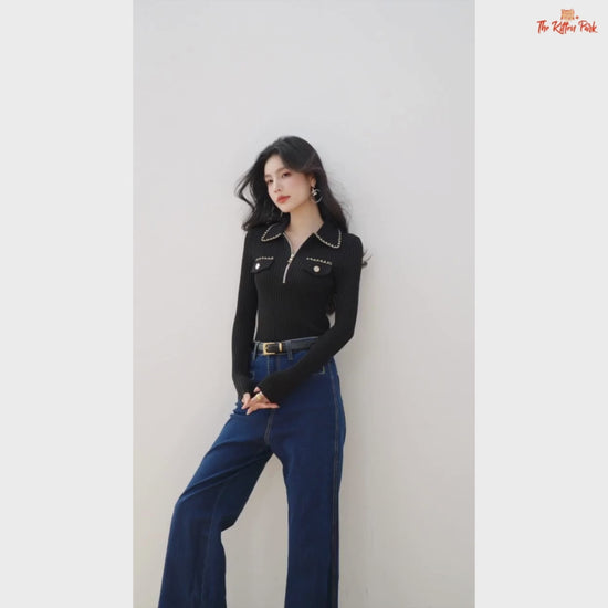 Woman wearing a black ribbed sweater with chain details and blue jeans on a beige background