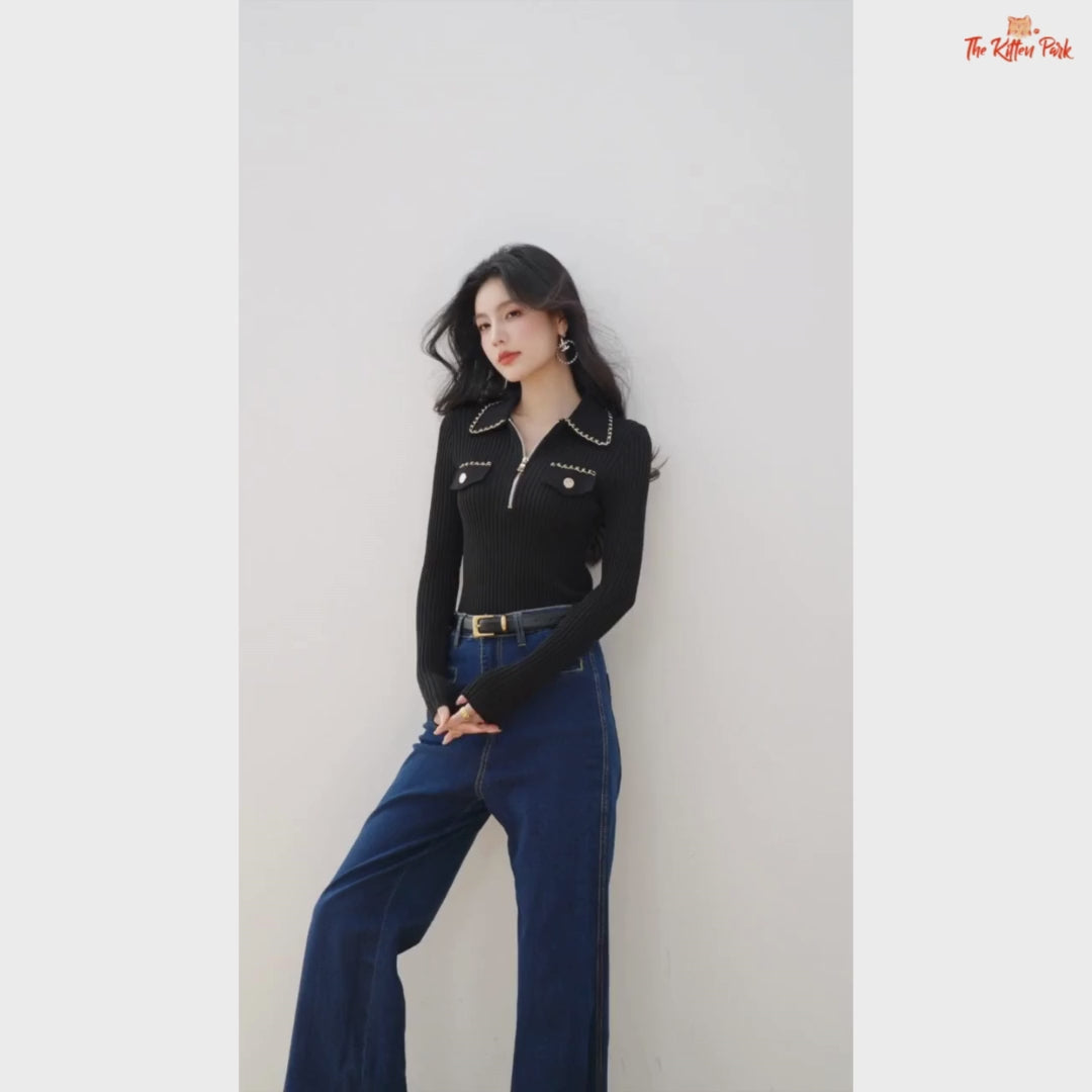 Woman wearing a black ribbed sweater with chain details and blue jeans on a beige background