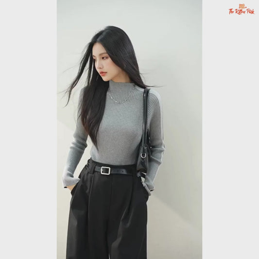 Woman wearing a gray ribbed sweater and black pants against a plain background