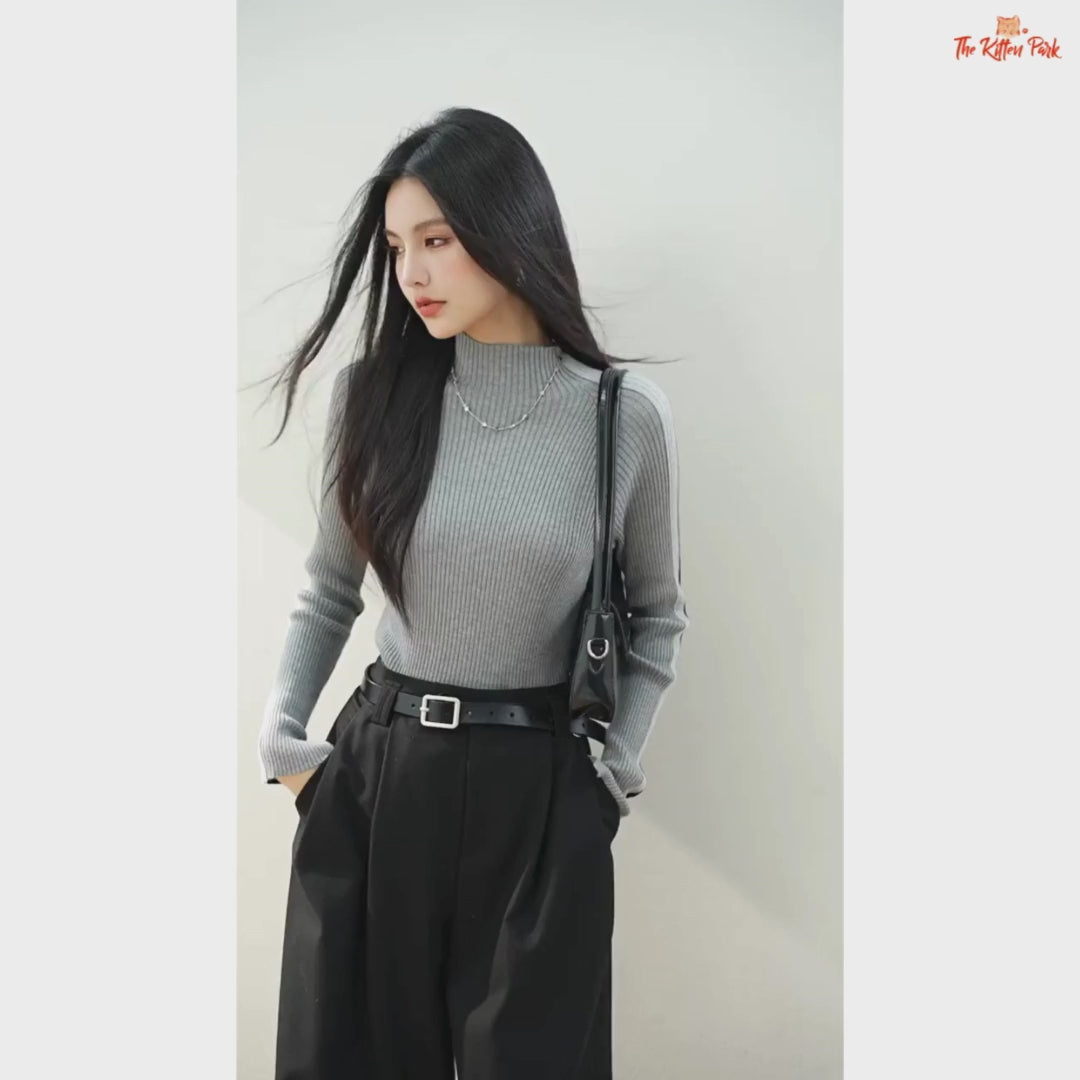 Woman wearing a gray ribbed sweater and black pants against a plain background